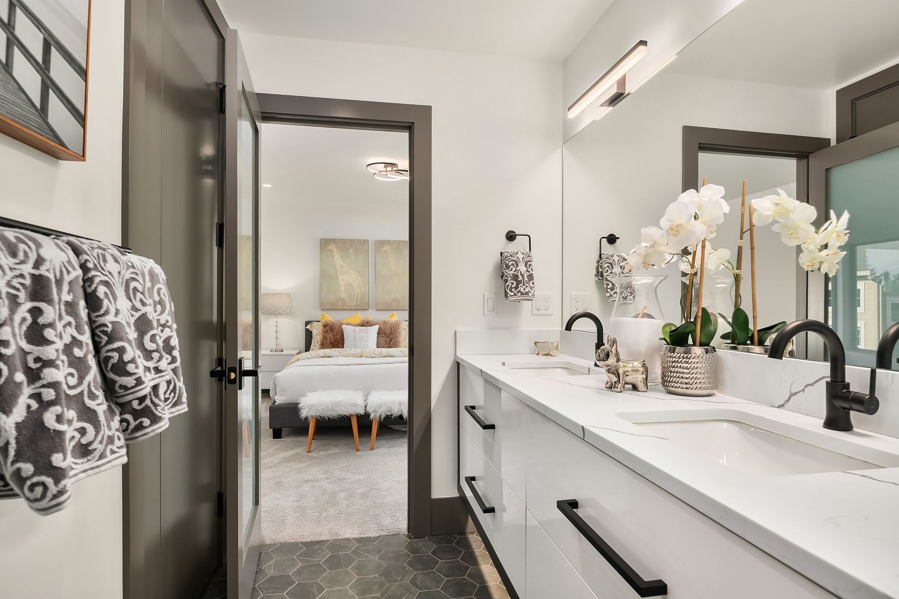 Bathroom with a white double vanity, black hardware, and an open door leading to a bedroom.