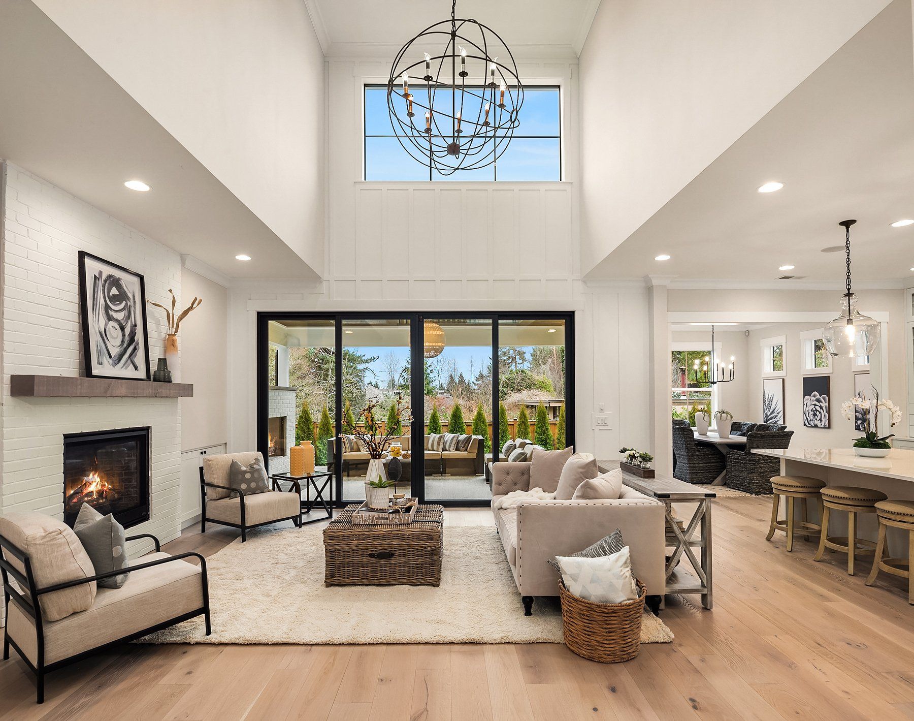 Spacious living room with fireplace, large window, and outdoor view. Neutral tones, light wood floor, and modern furniture.