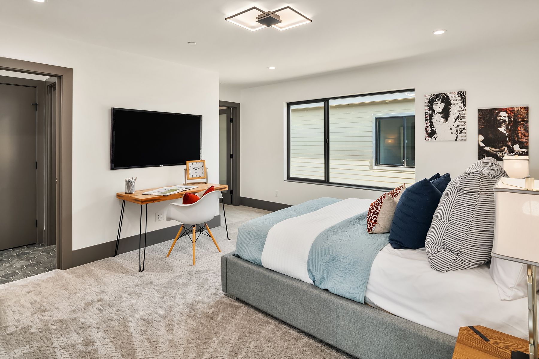 Bedroom with a bed, desk, and a large TV, with art on the wall and a window.