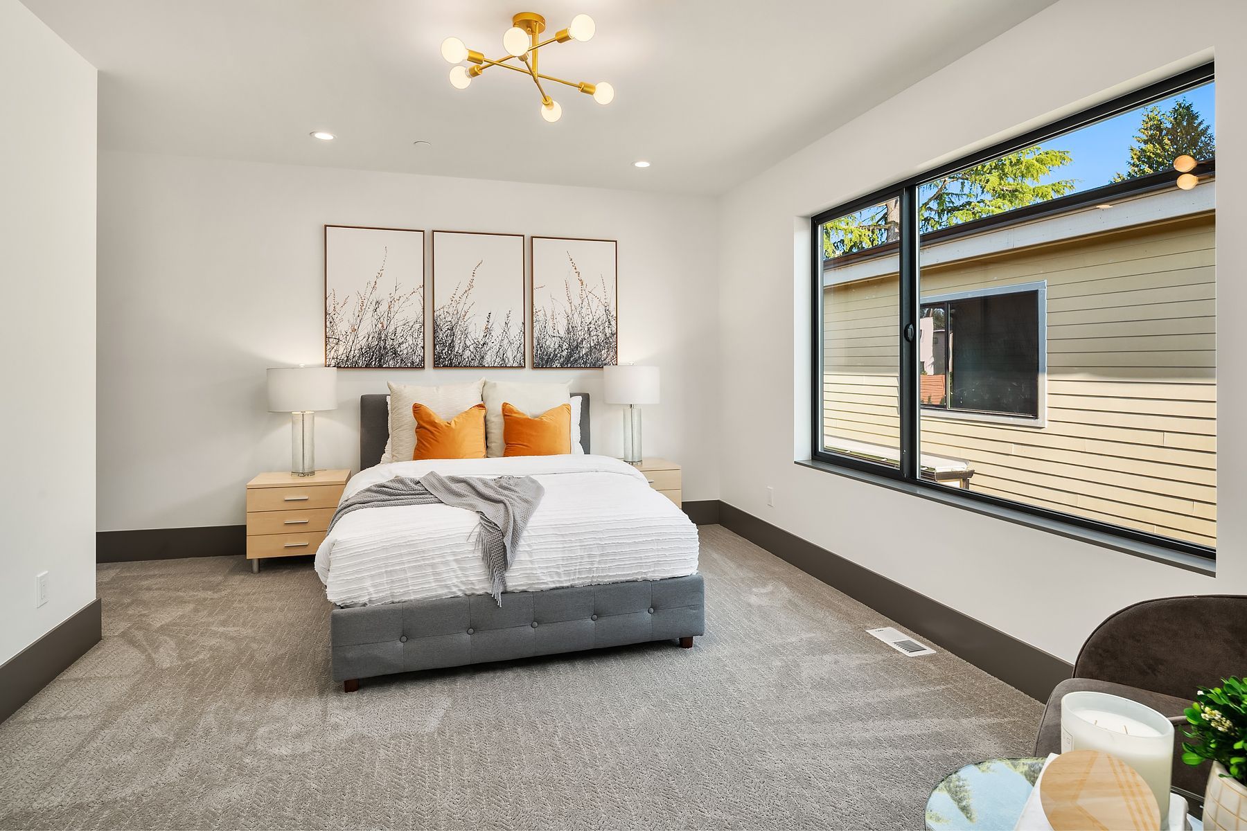 Bedroom with gray bed, orange pillows, art, and large window.