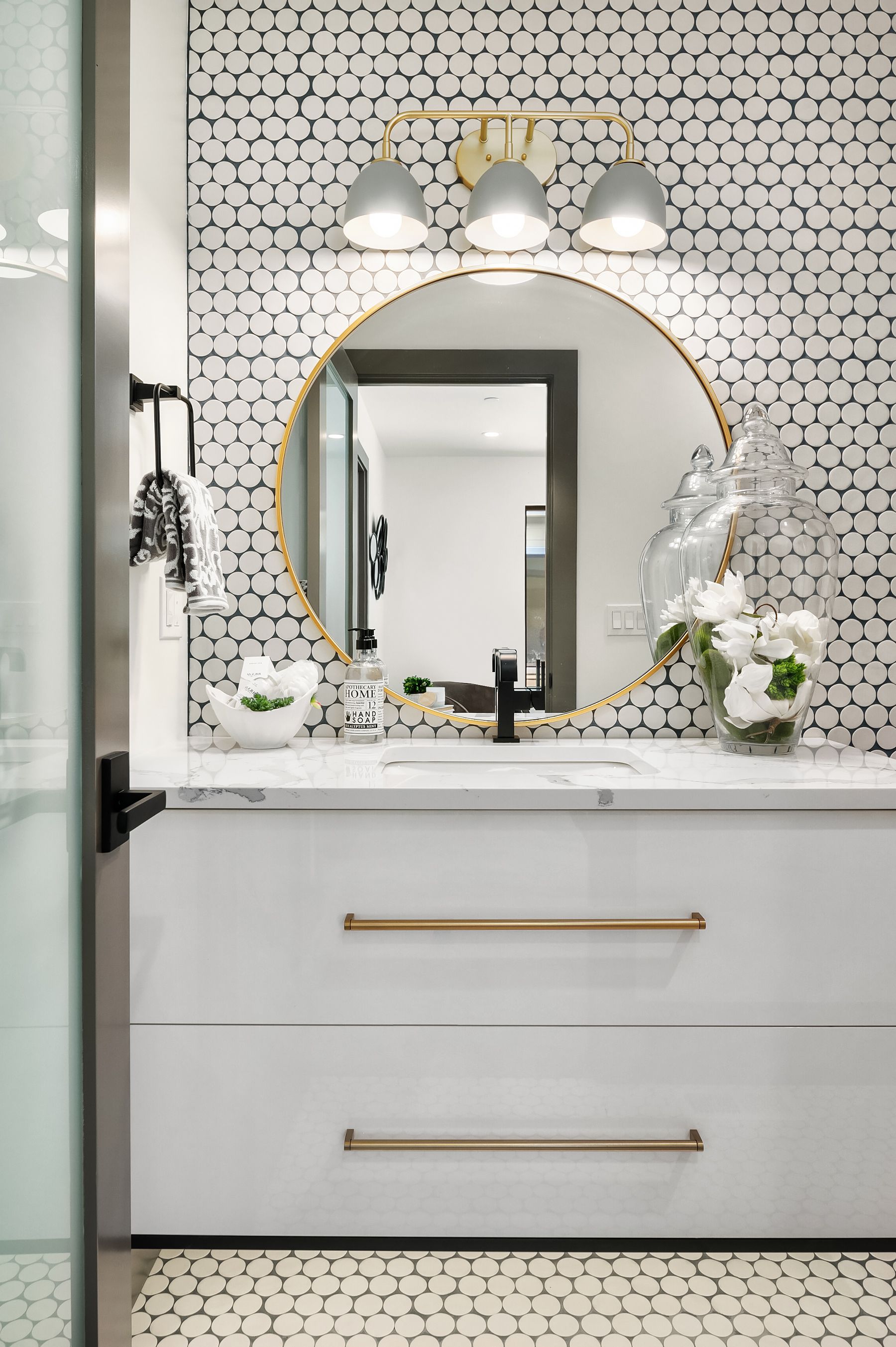 Bathroom vanity with patterned wallpaper, a gold-framed mirror, white countertop, and gold hardware.