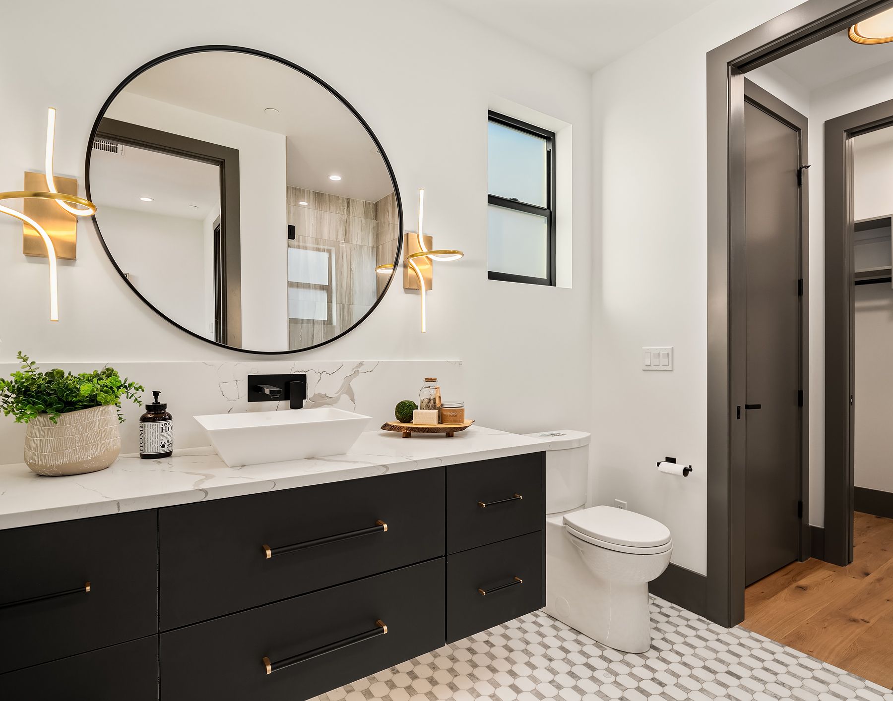 Modern bathroom with a black vanity, round mirror, and gold sconces.