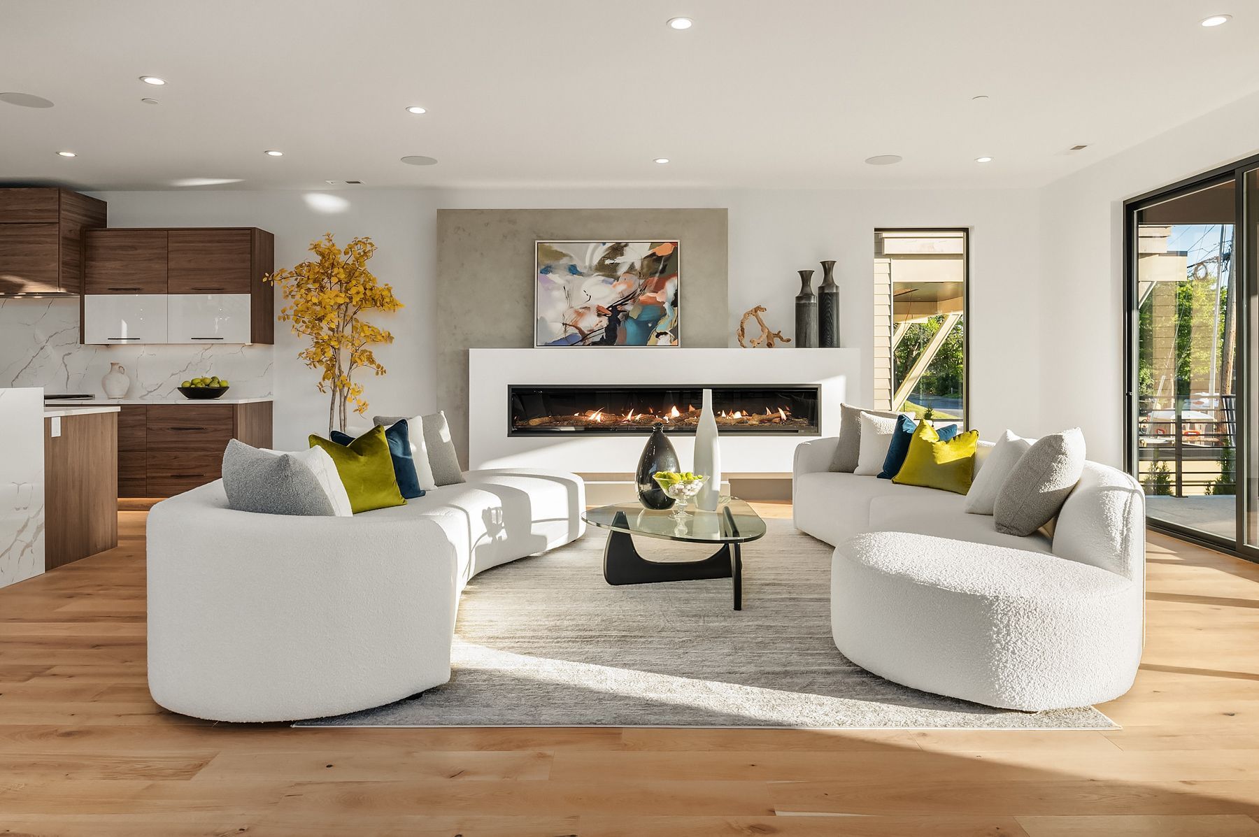 Modern living room with white curved sofas, fireplace, and open kitchen.