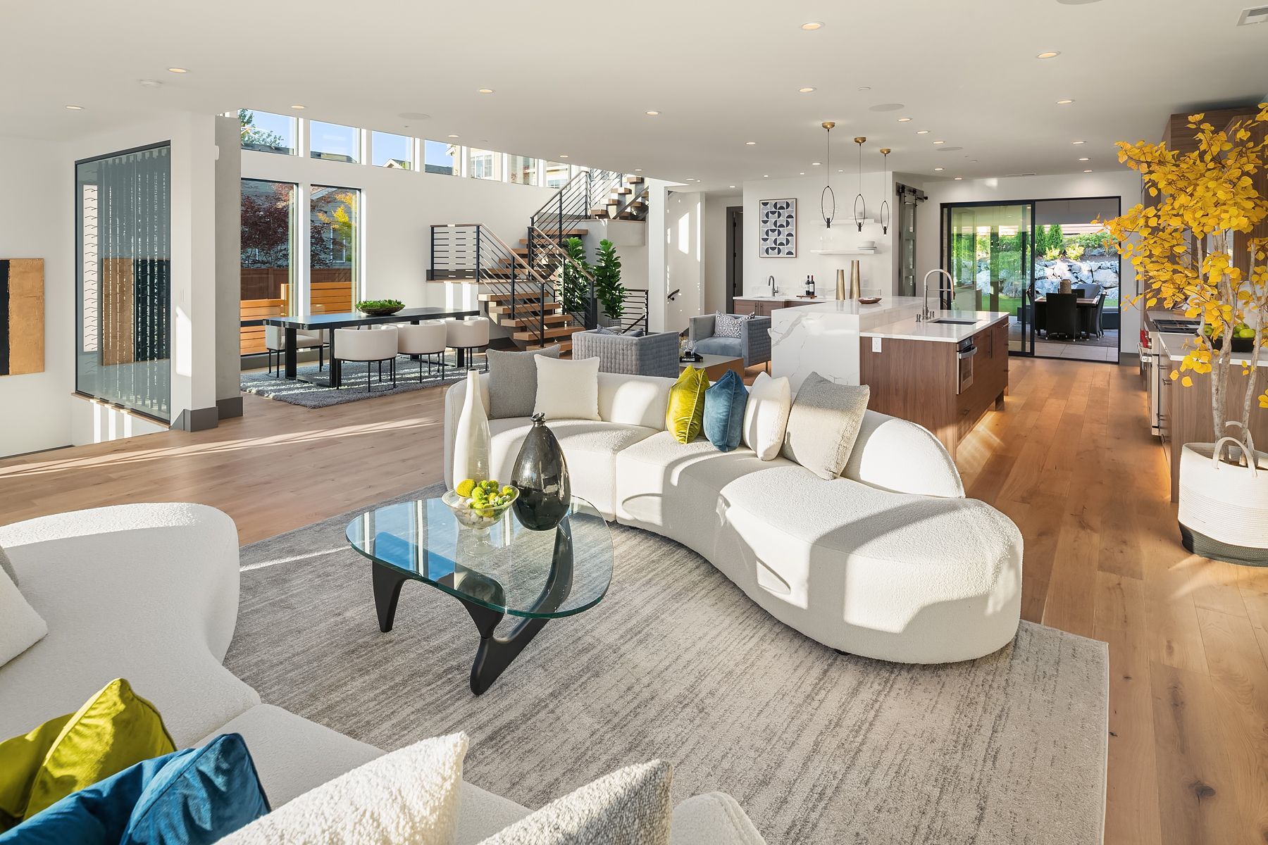 Spacious modern living room with white sofa, light wood floors, and dining area visible.