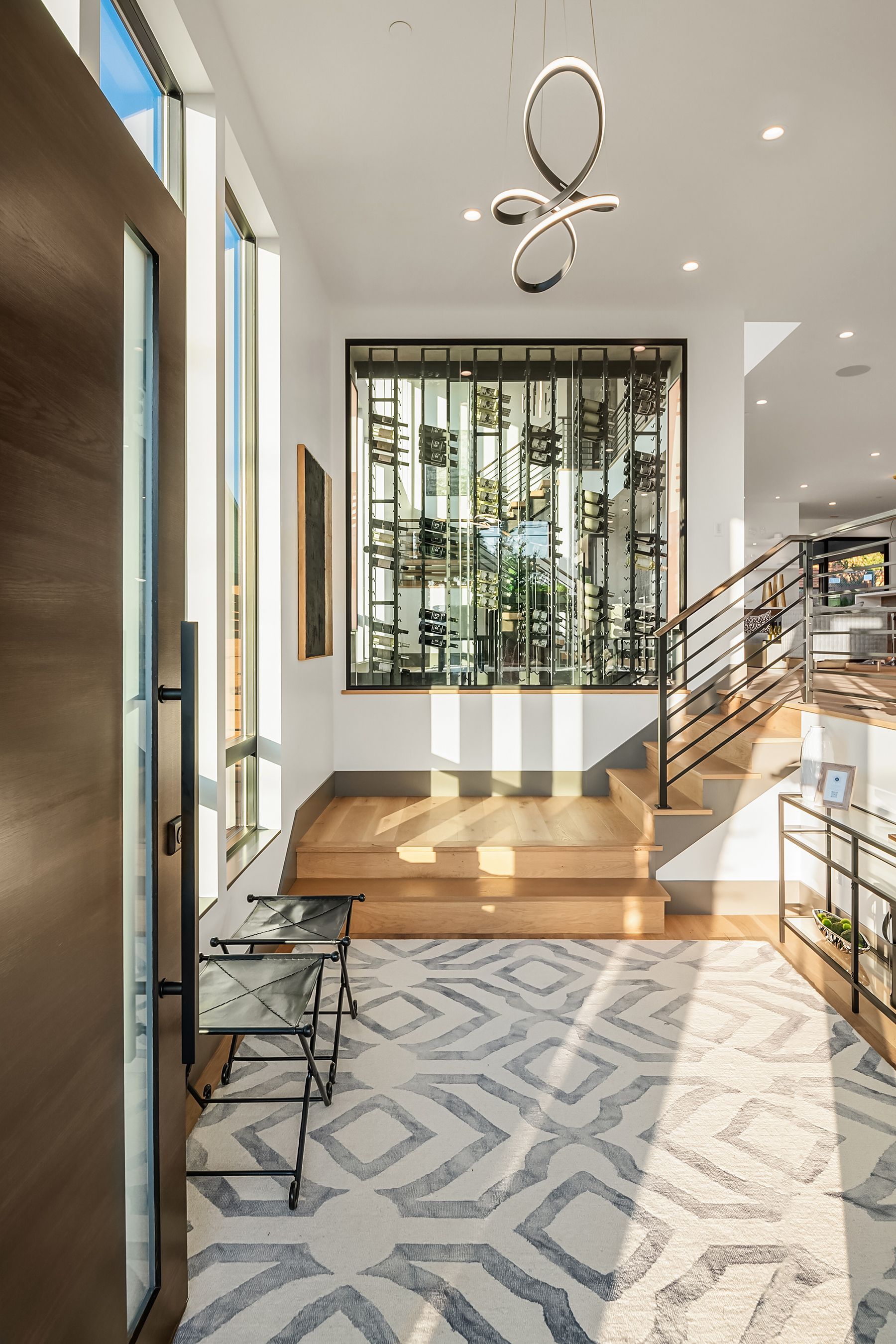 Modern home entryway with a wine cellar, hardwood stairs, and patterned rug.