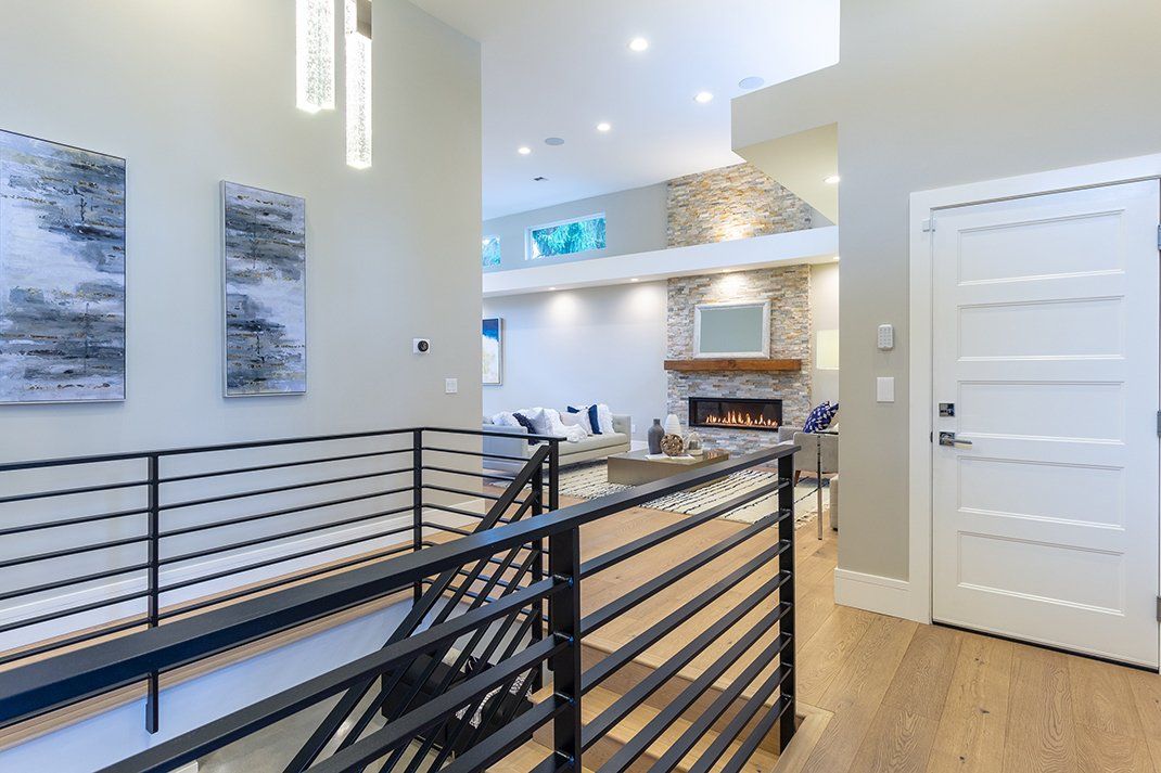 Hallway with black railing, artwork, and view of living room with fireplace.