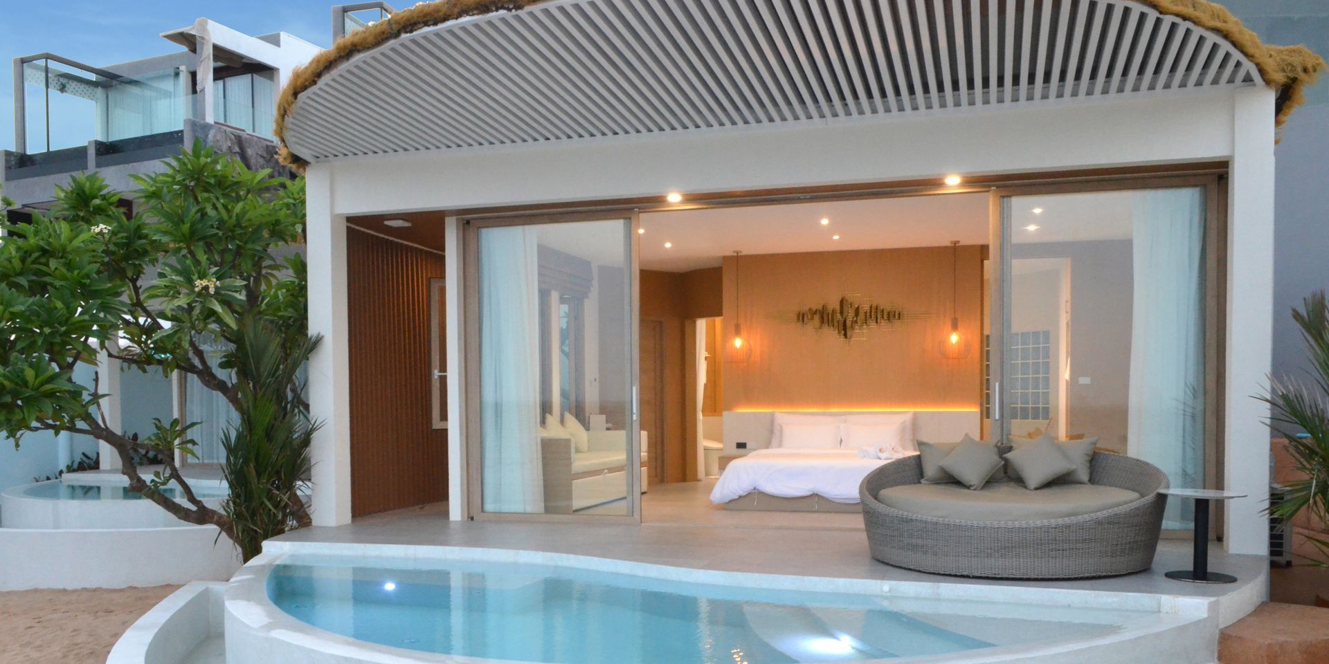 Luxury resort room with a pool, open doors, and a round outdoor seating area.
