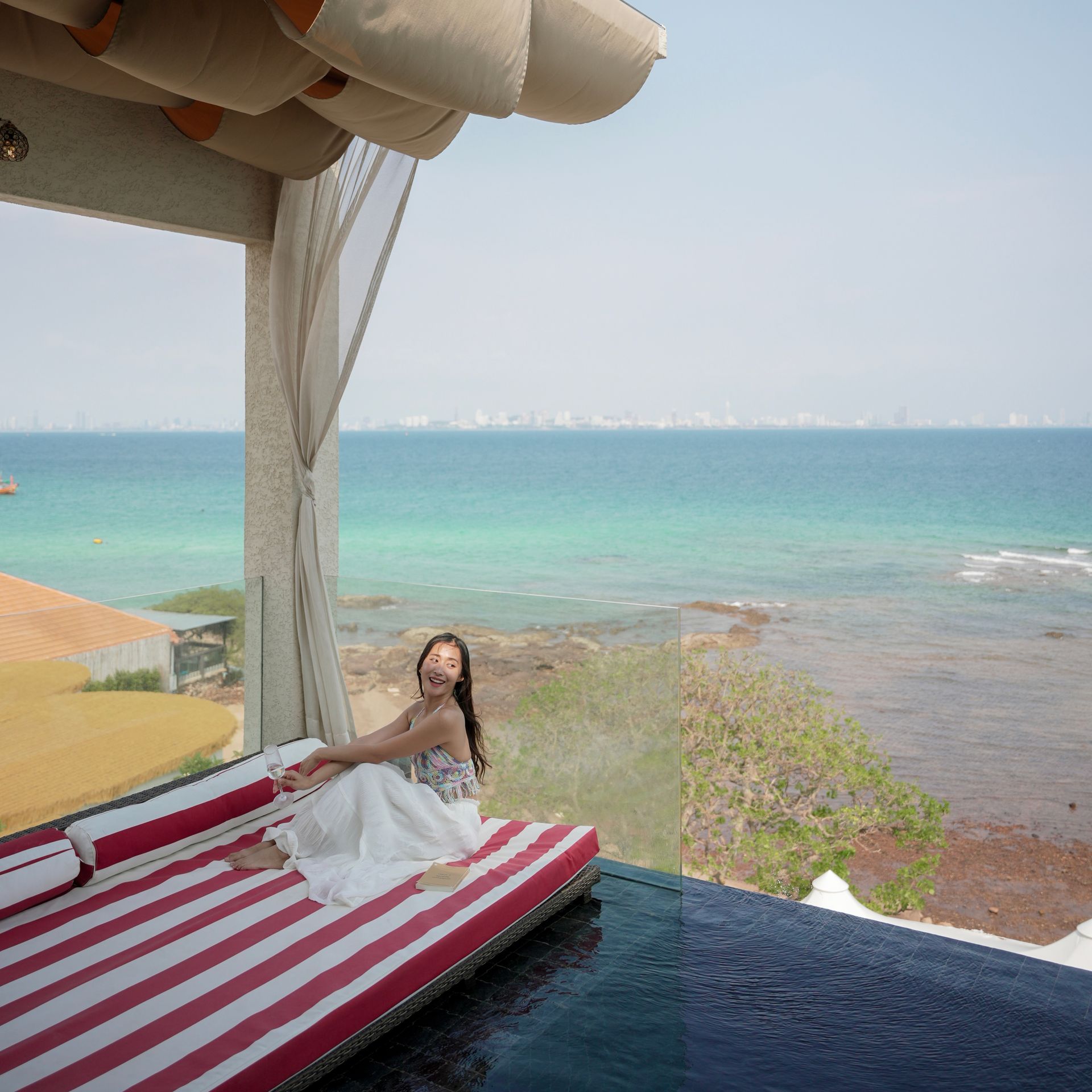 Woman sits on striped lounge, ocean view.
