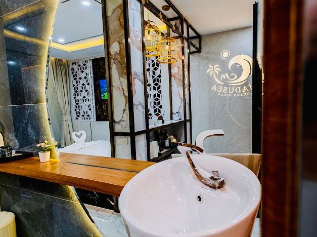 Bathroom with white sink, brown wooden counter, gold light fixture, and marble wall decor.