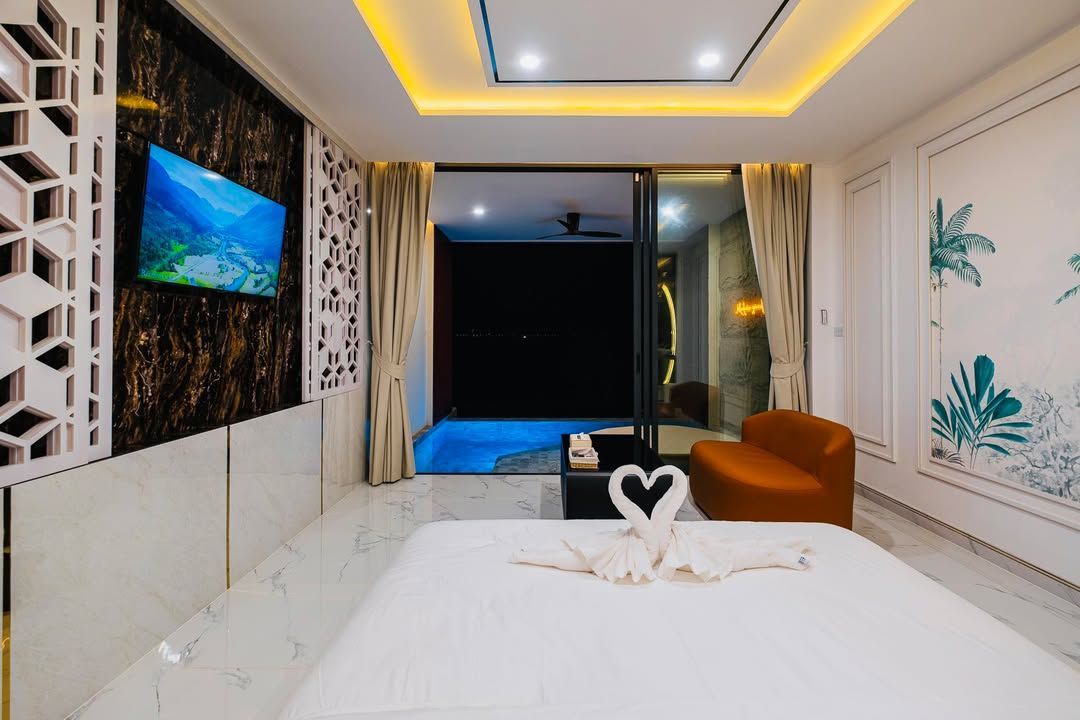 Luxury bedroom with pool view, white bed, TV, orange chair, and patterned wall.