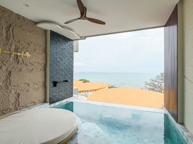A luxurious hotel room with a private pool overlooking the ocean. Features a round bed, stone walls, and a ceiling fan.