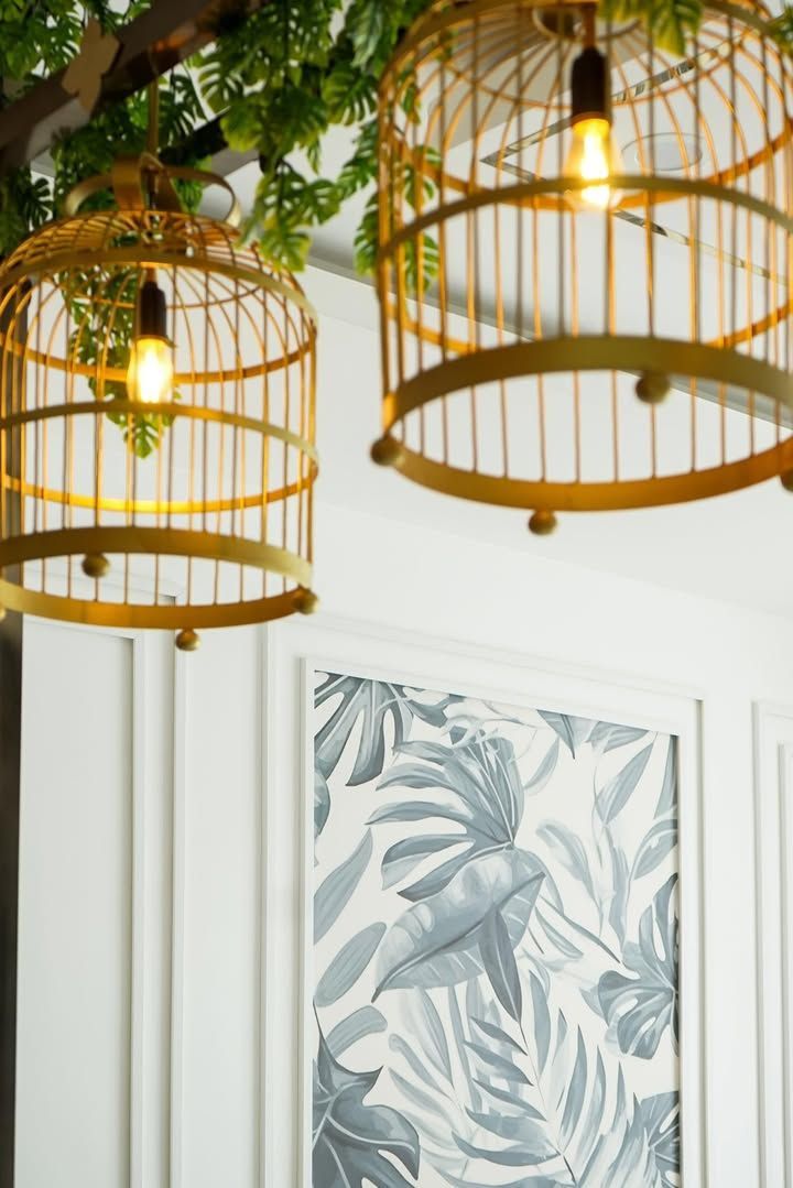 Gold birdcage light fixtures, leafy wallpaper, white wall.
