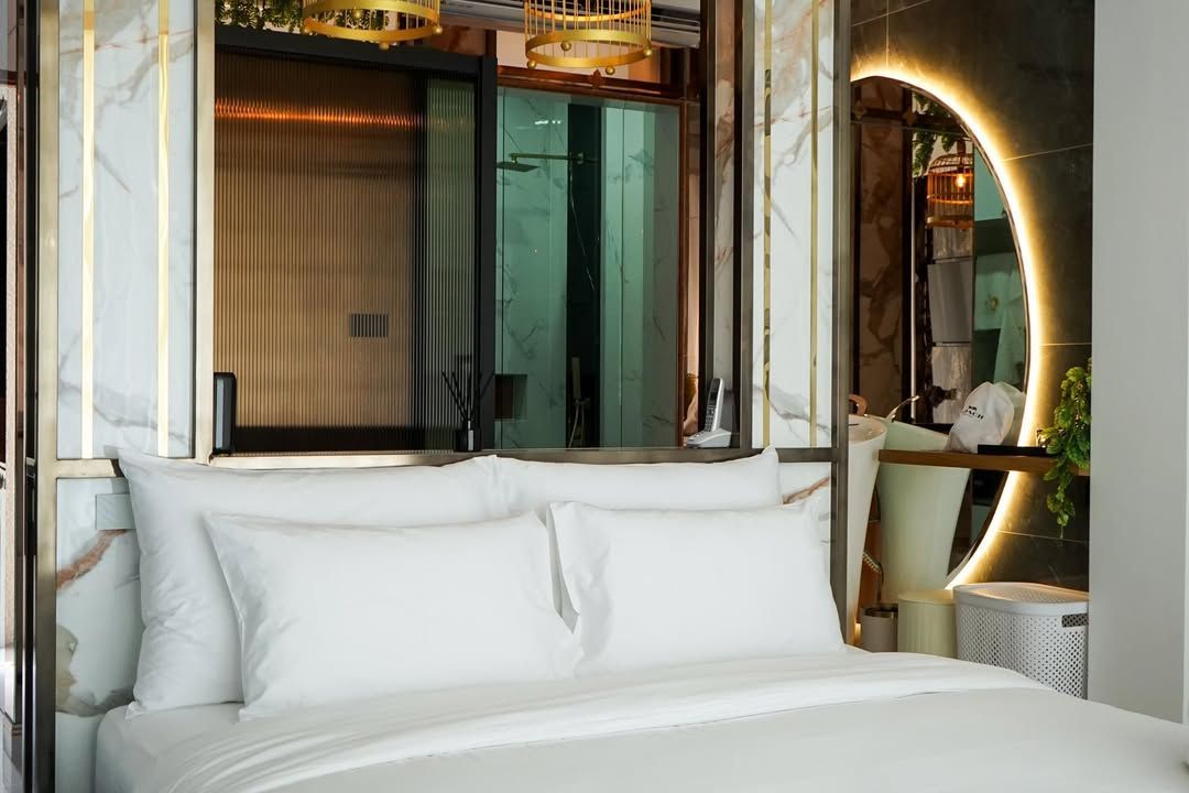 Bedroom with white bedding, marble wall, gold accents, and a mirror with a circular illuminated frame.