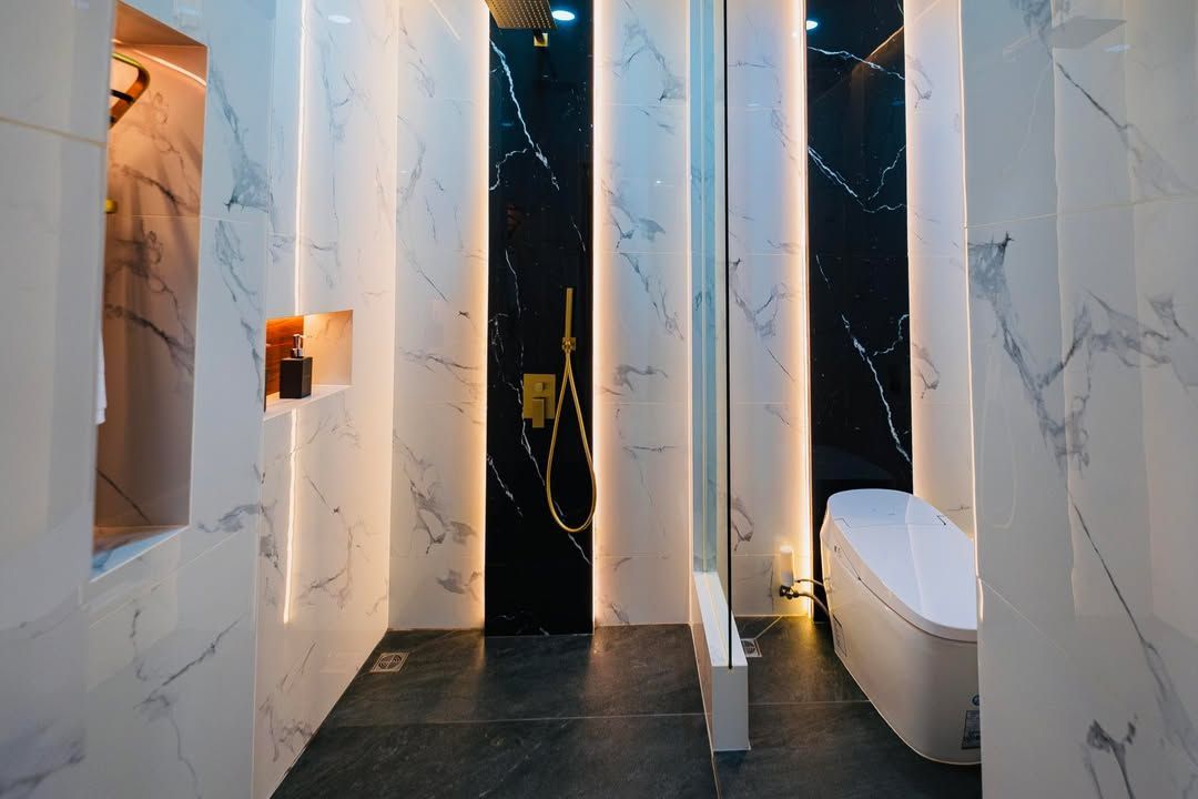 Bathroom with marble walls and black accent wall, shower area with gold fixtures and tub.