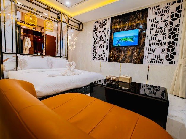 Bedroom with a bed, orange chaise lounge, black coffee table, TV on the wall, and decorative wall panels.