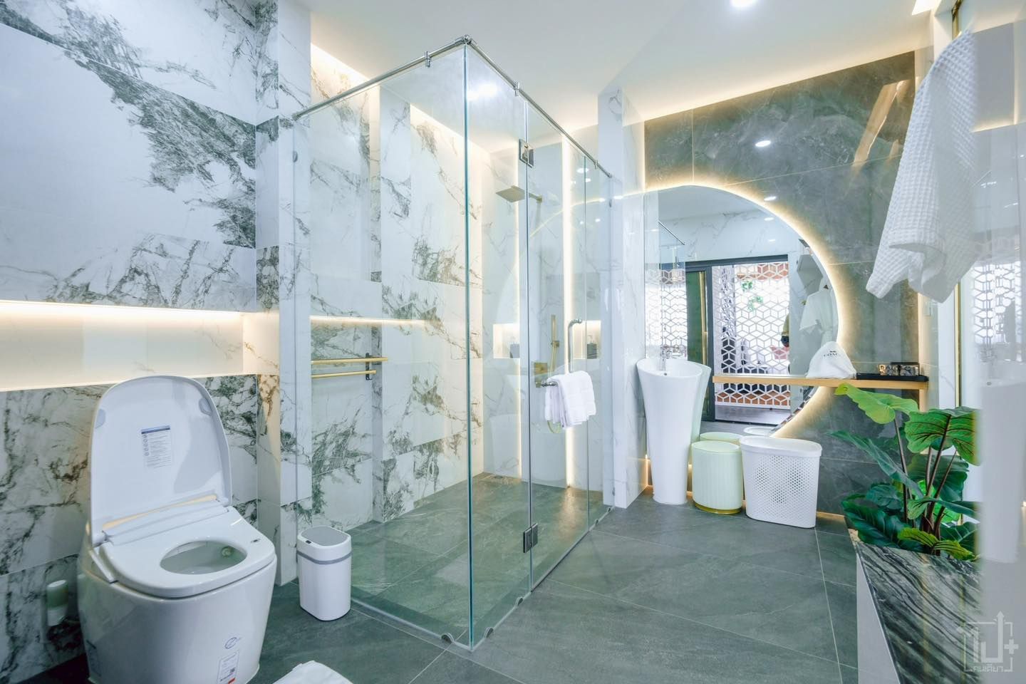 Modern bathroom with marble walls, glass shower, toilet, sink, and decorative lighting.