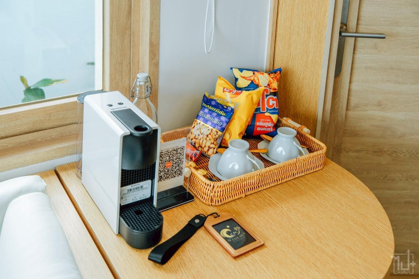 A hotel room coffee station. Espresso machine, snacks, cups, and a wooden table.