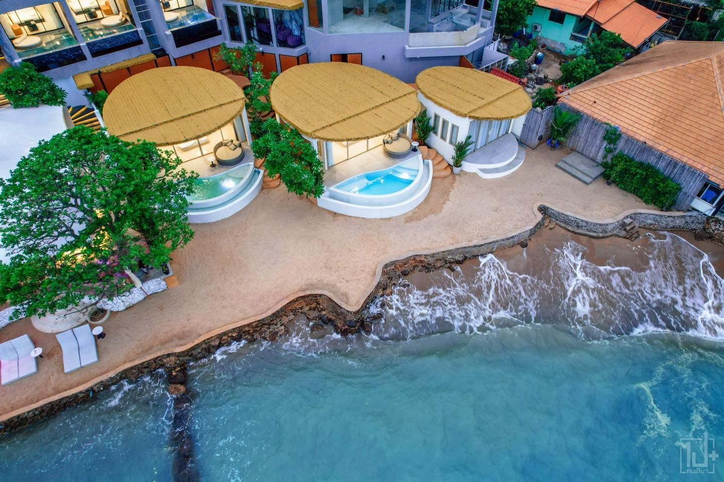 Aerial view of three beachside huts with private pools, sandy shore, and turquoise water.