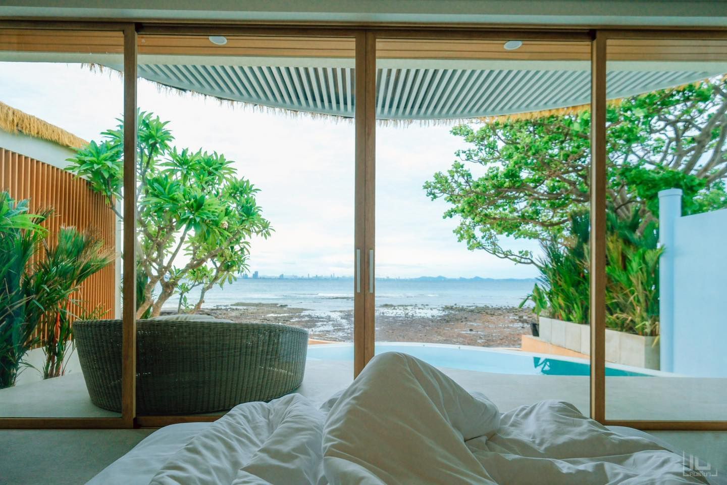 Bedroom with ocean view through large windows; bed with rumpled white linens.