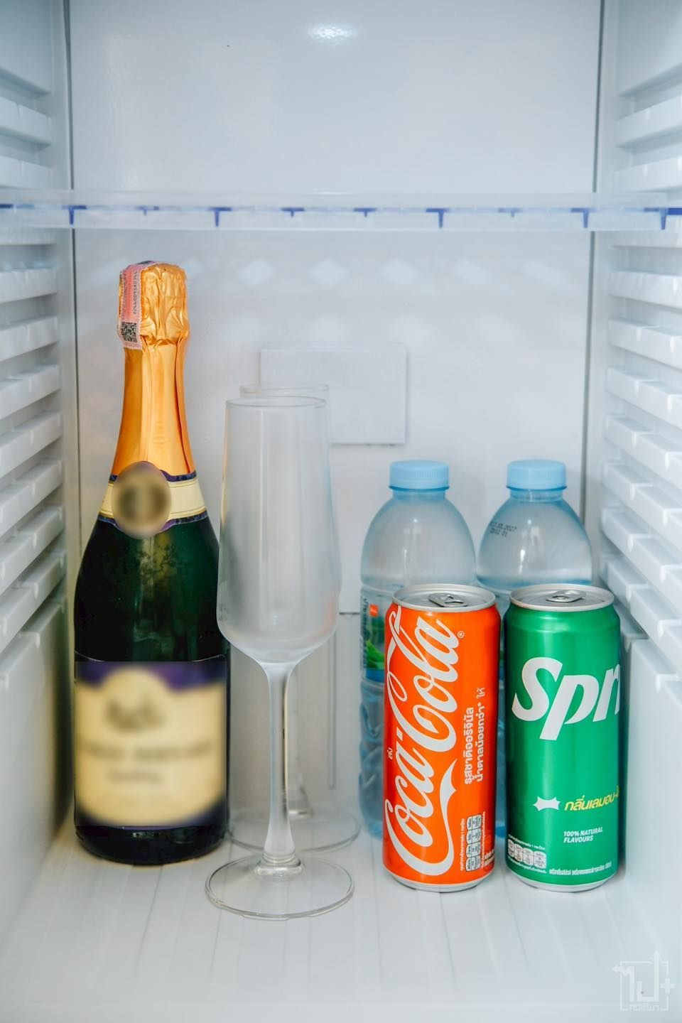 A refrigerator interior with champagne bottle, champagne glass, soda cans, and water bottles.
