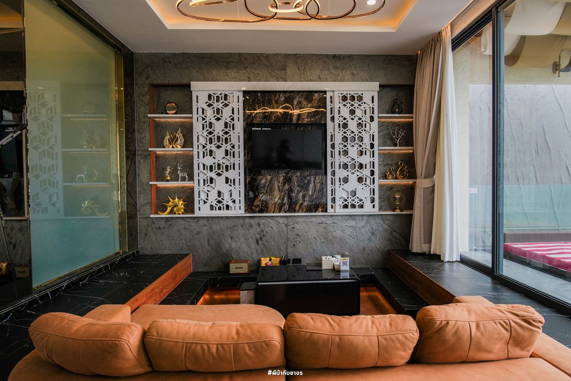 Living room with brown sectional sofa, TV, shelves with decor, and large window.