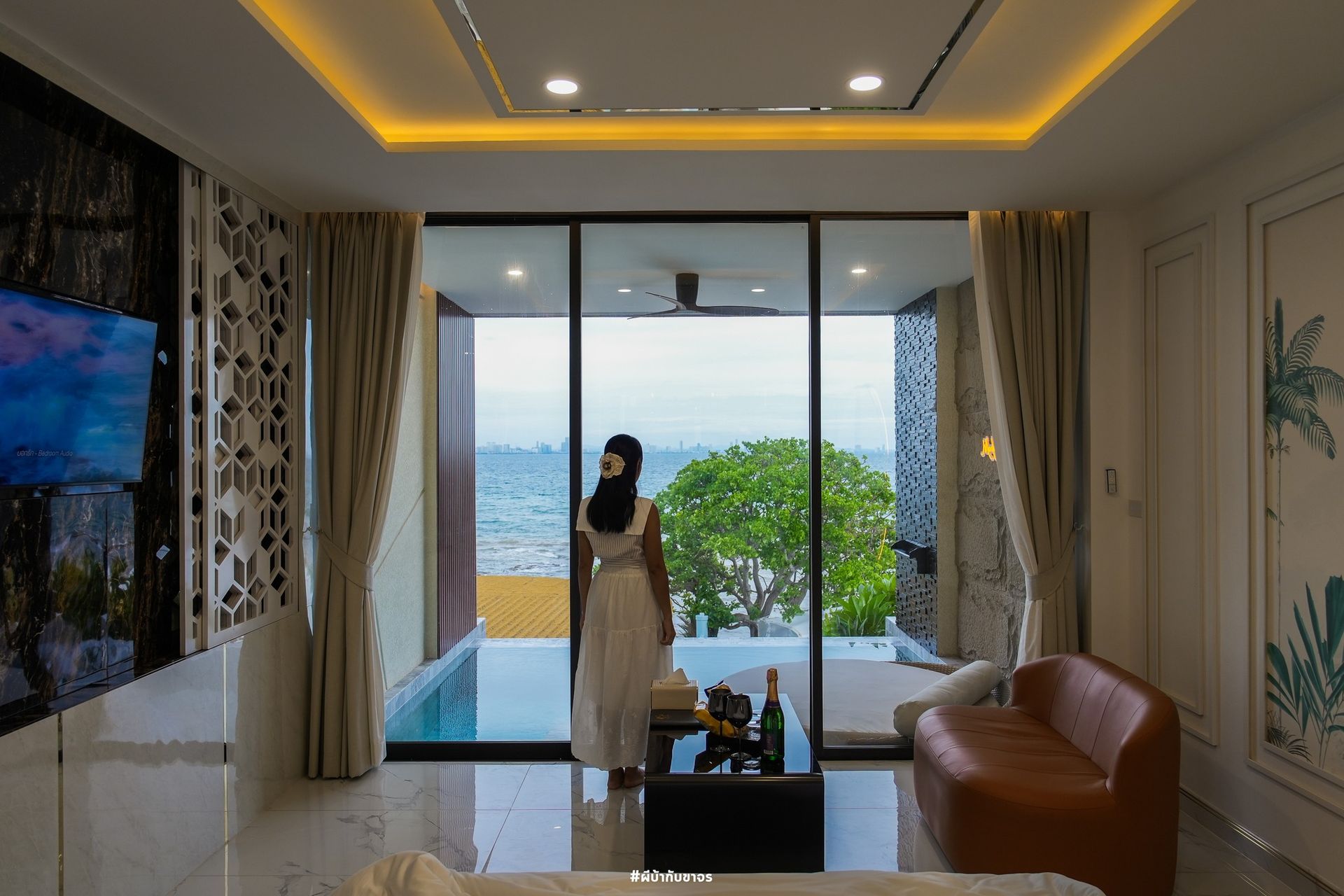 Woman in white dress standing near an open doorway overlooking the ocean, inside a modern room.