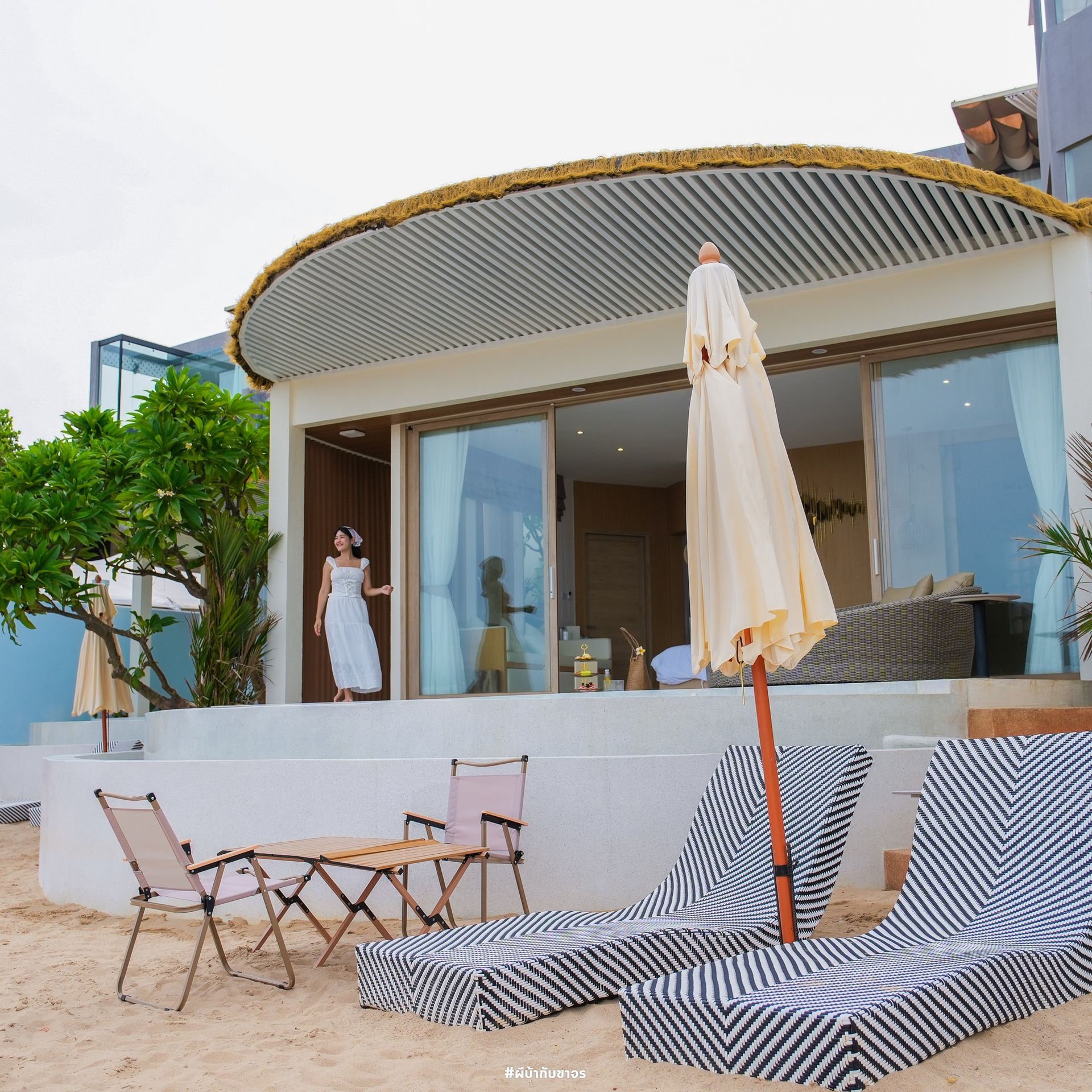 Woman standing on a patio overlooking beach chairs and ocean. Beach house with open glass doors.