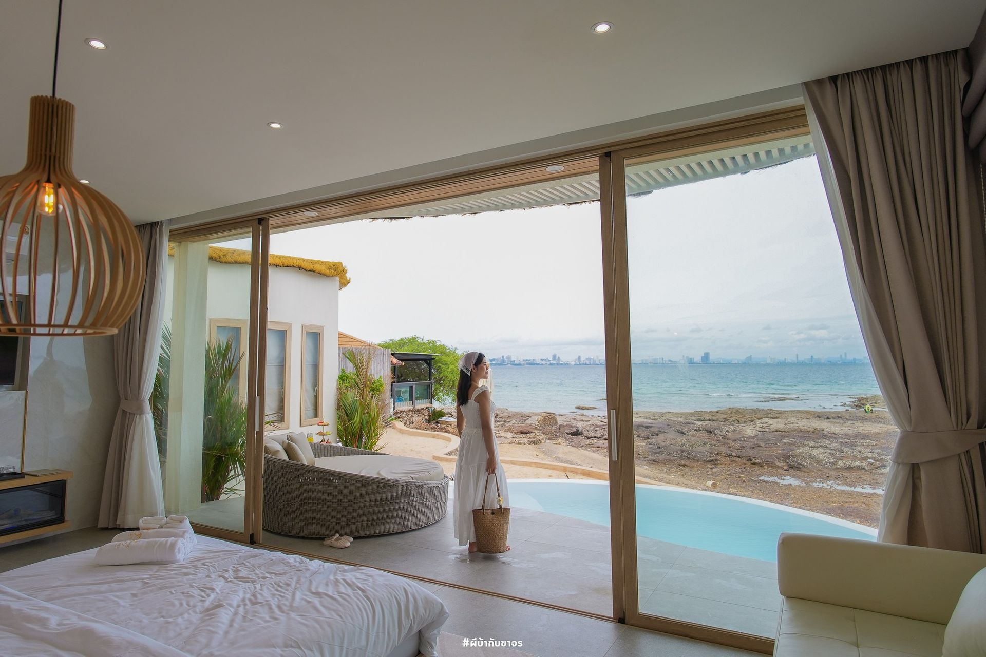 Woman standing by large window overlooking ocean; indoor-outdoor living, modern design.