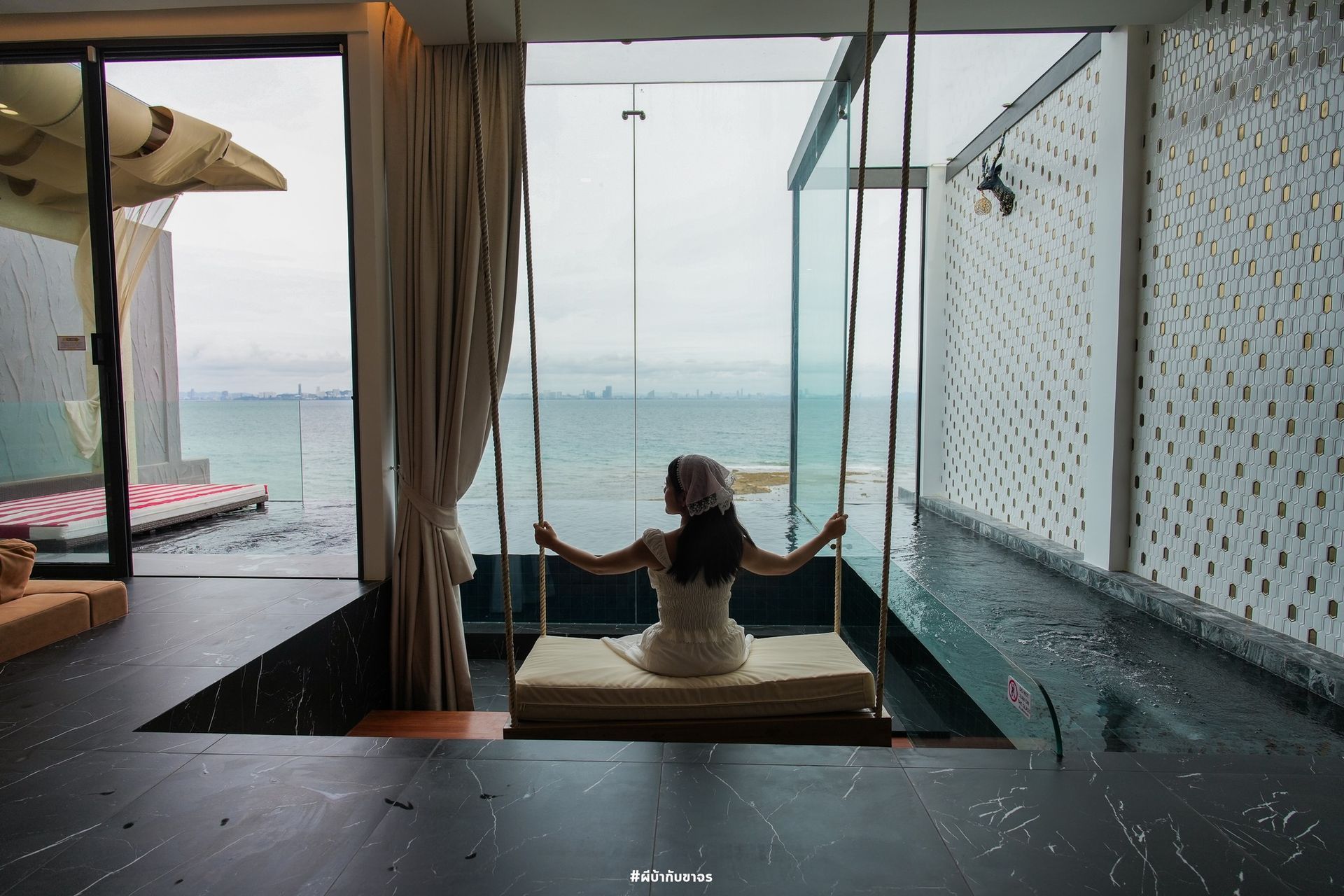 Woman on a swing over a pool with an ocean view; neutral tones and natural light.