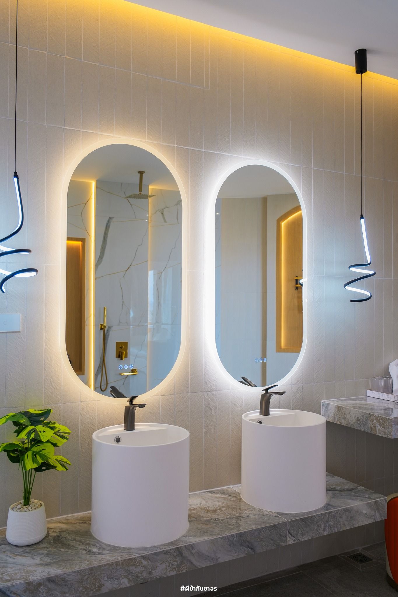 Modern bathroom with two illuminated oval mirrors, white sinks, and decorative lighting.