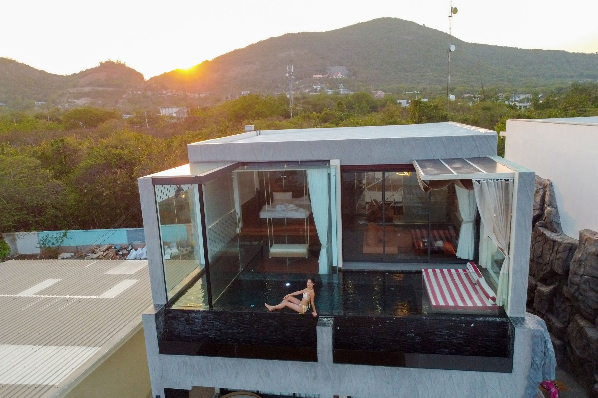 Woman relaxing in rooftop pool, glass-walled room, mountain sunset.