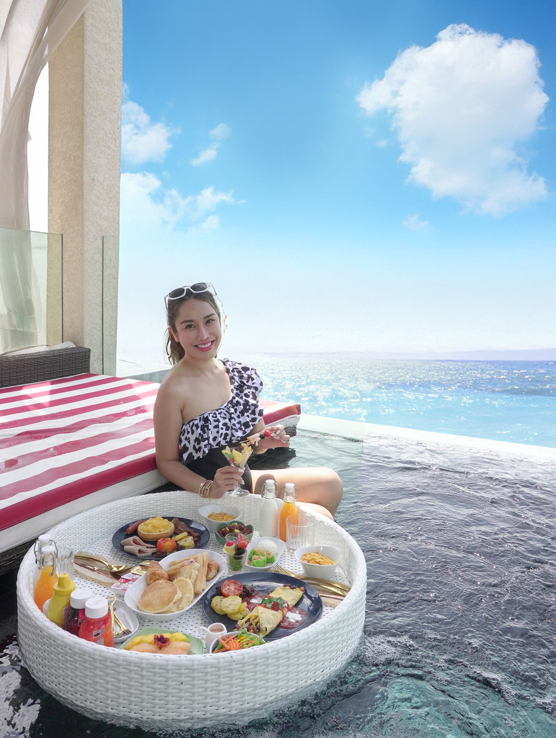 Woman enjoying floating breakfast in pool, overlooking ocean, clear sky.