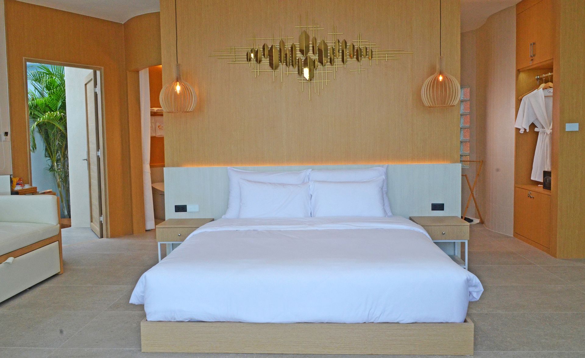 Bedroom with a bed, nightstands, and a modern light fixture. Beige walls and a door lead to an outdoor view.