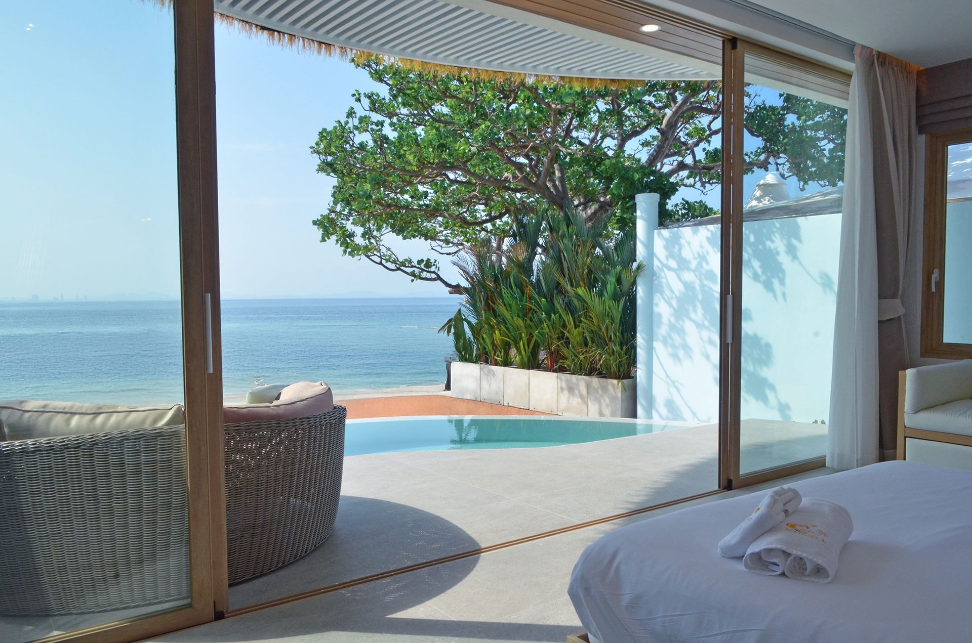 Open doorway reveals ocean view, private pool, and outdoor seating. Bright natural light floods the room.