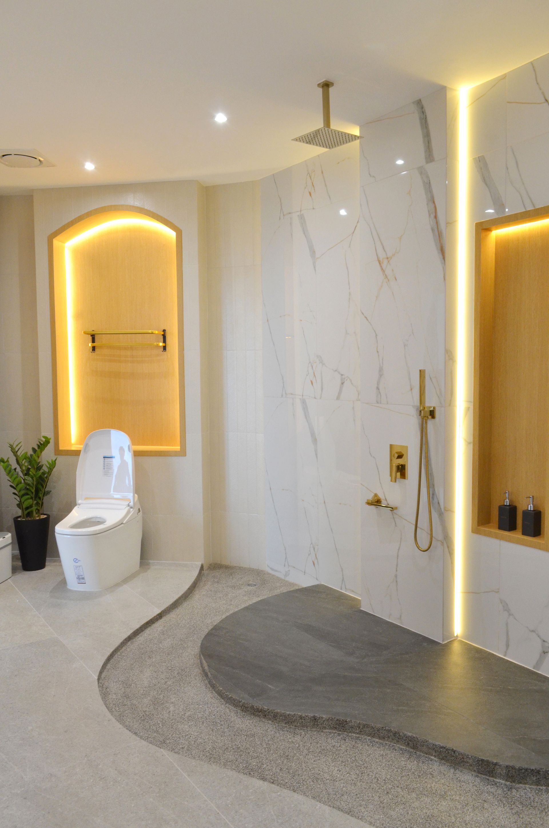 Modern bathroom with marble shower, gold fixtures, and curved floor design.