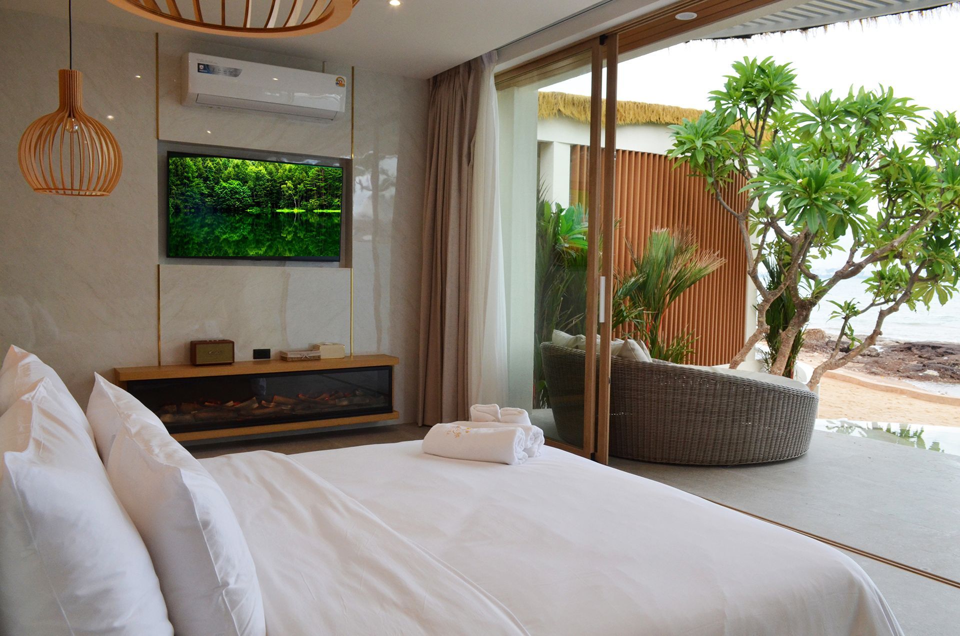 Bedroom with a large bed, TV, and open sliding door to a patio with outdoor seating near the ocean.