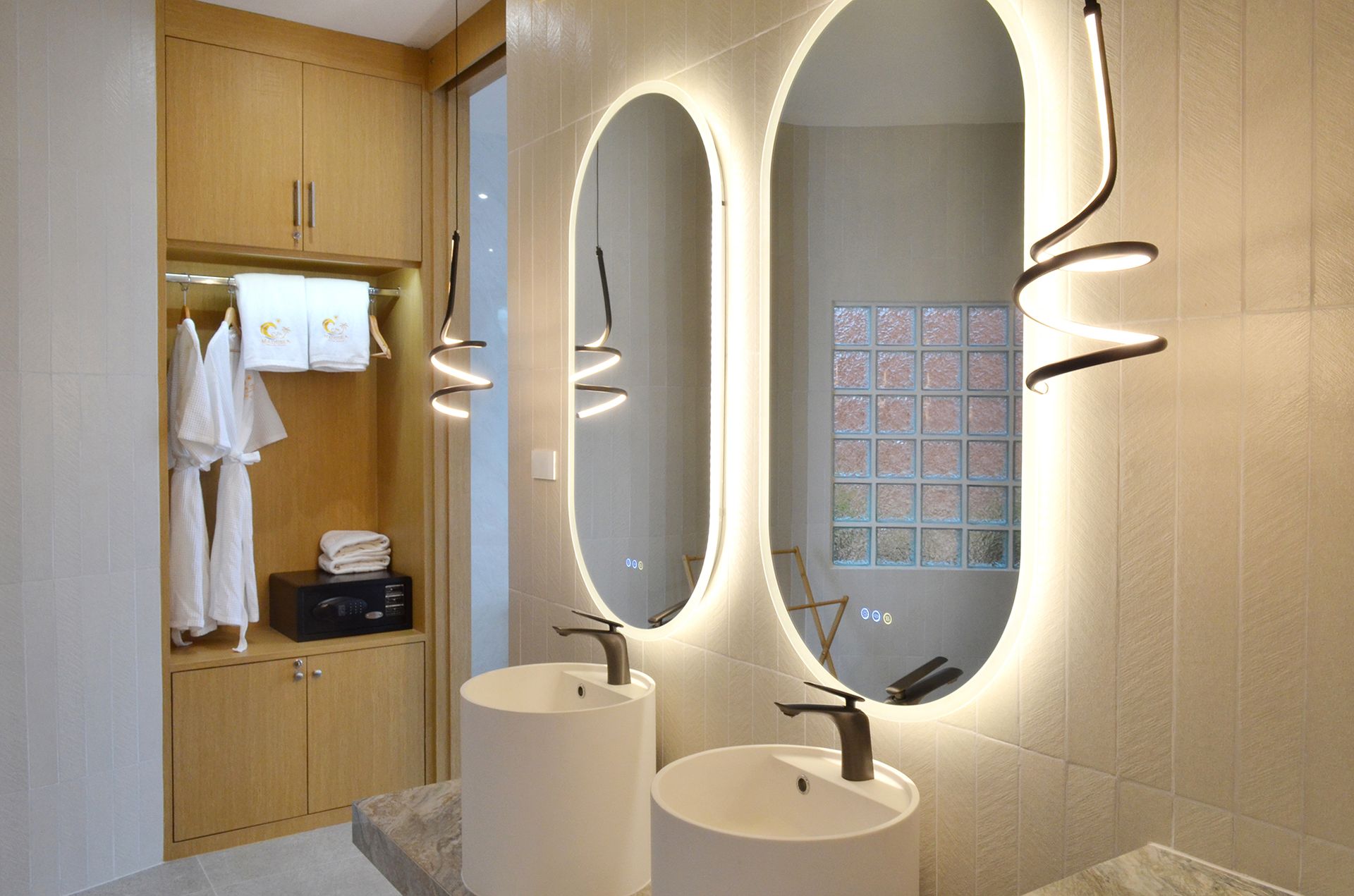Modern bathroom with two illuminated oval mirrors above white sinks, and wooden closet.