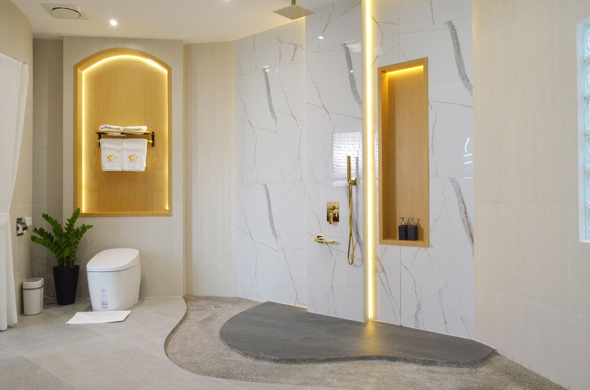 Modern bathroom with marble shower, gold accents, and a unique stone floor design.