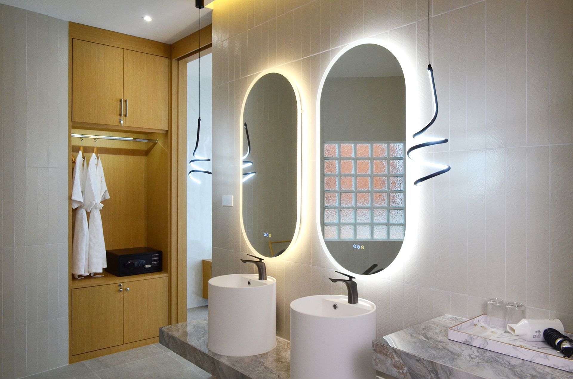 Modern bathroom with illuminated oval mirrors above white sinks, and wooden cabinet.