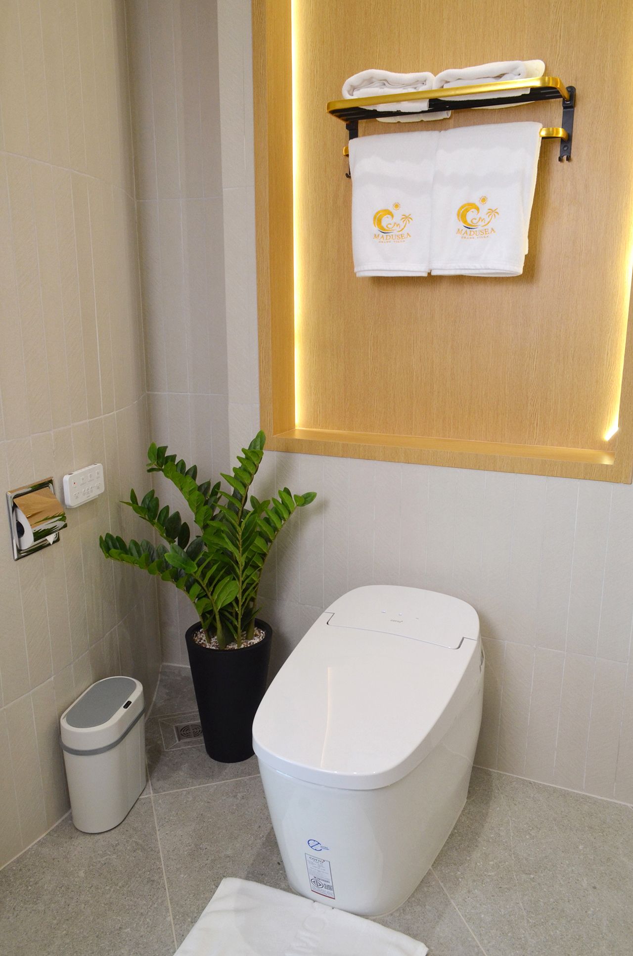 Bathroom with a white, modern toilet, towel rack, potted plant, and trash can.