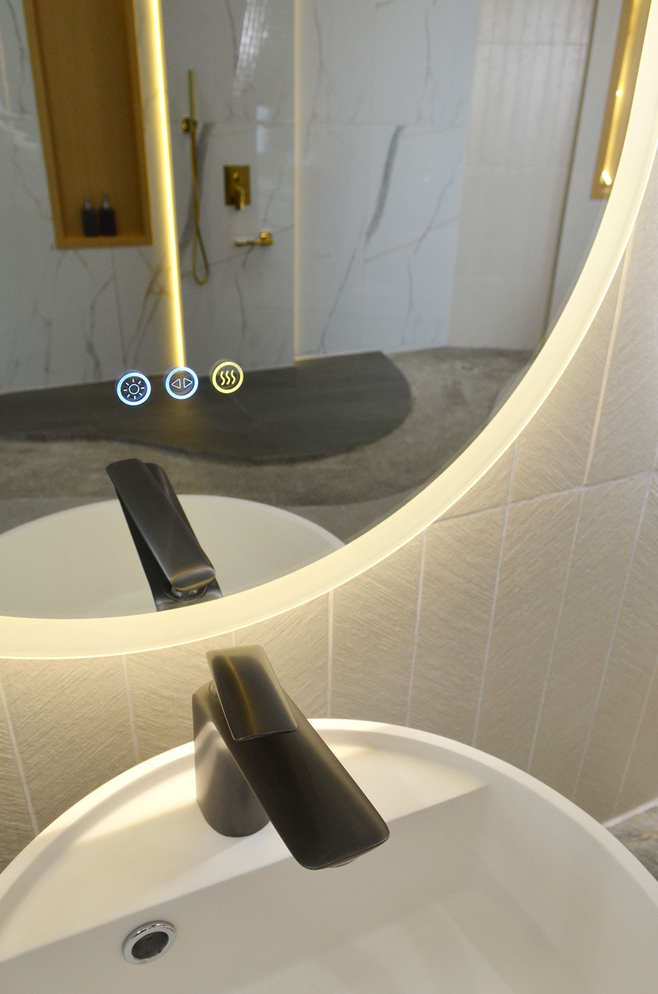 Bathroom mirror reflecting a sink, faucet, and shower fixtures; oval mirror with illuminated edges.