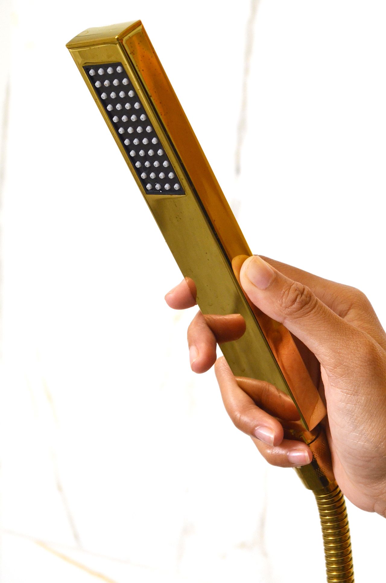 Hand holding a gold, rectangular showerhead with a black square of spray holes.