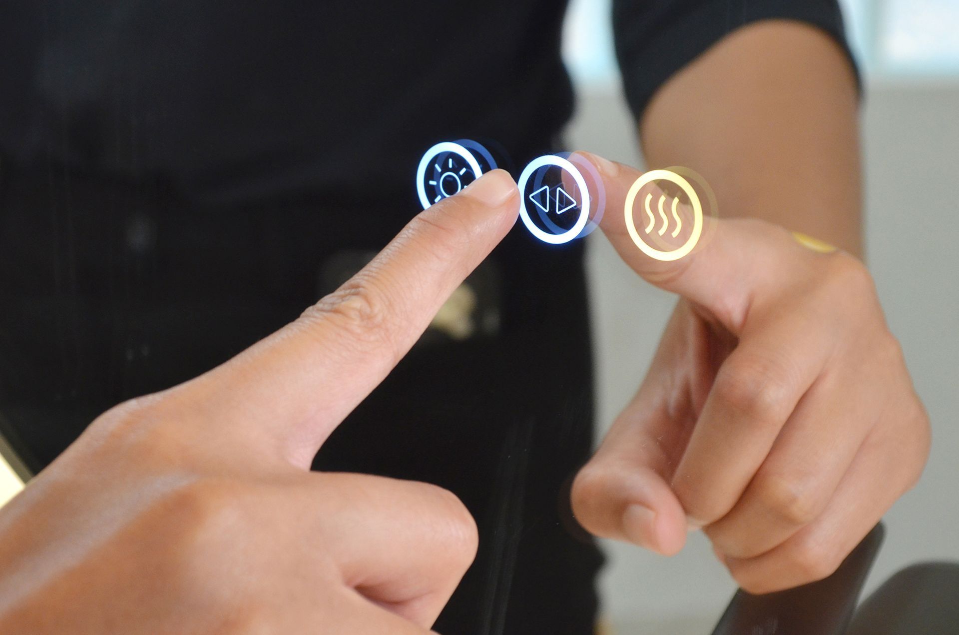 A person's finger touching illuminated touch controls on a mirror: light, settings, heat.