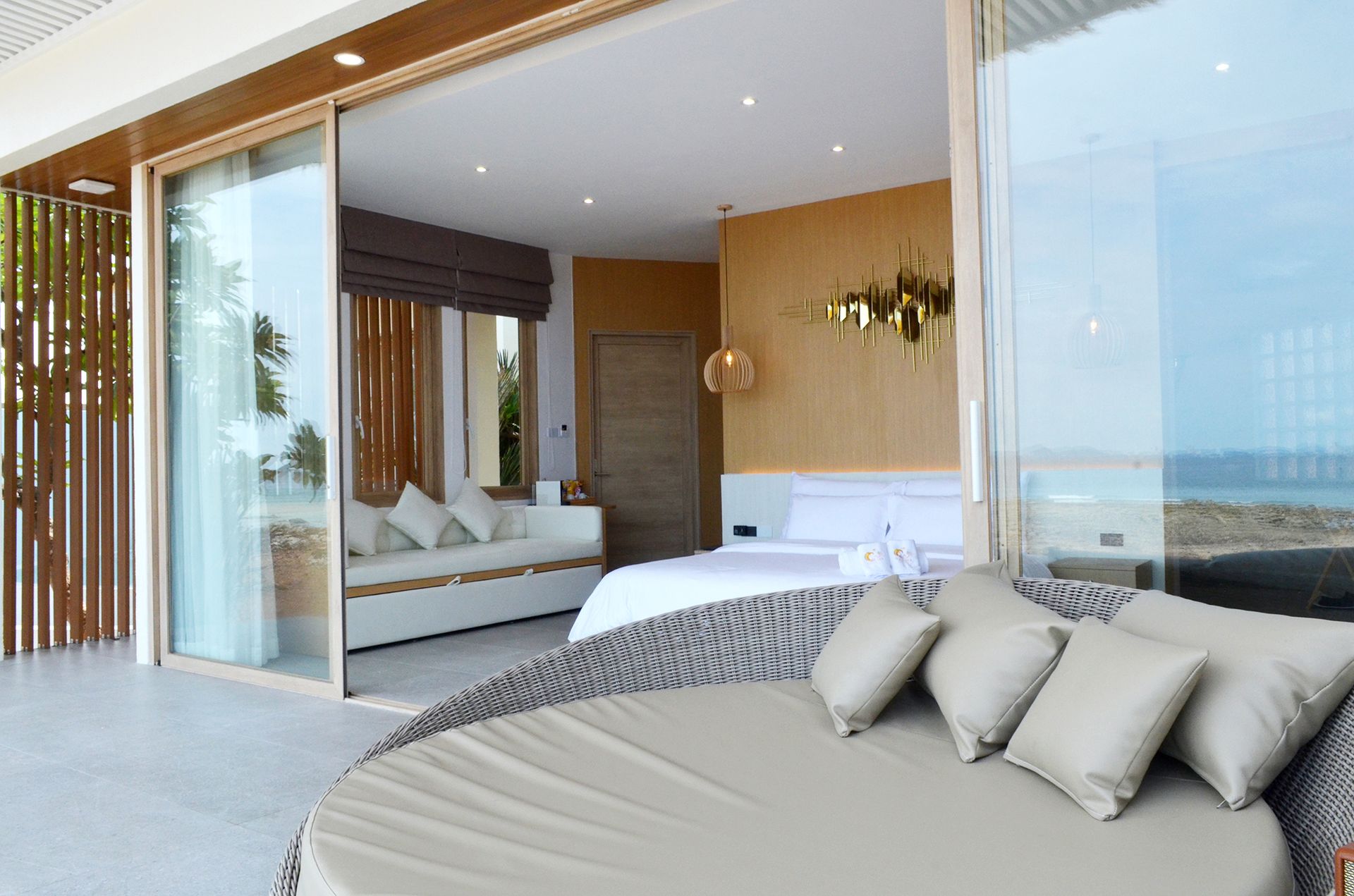 Bedroom with open sliding doors to a patio; round outdoor daybed, bed, sofa, ocean view.