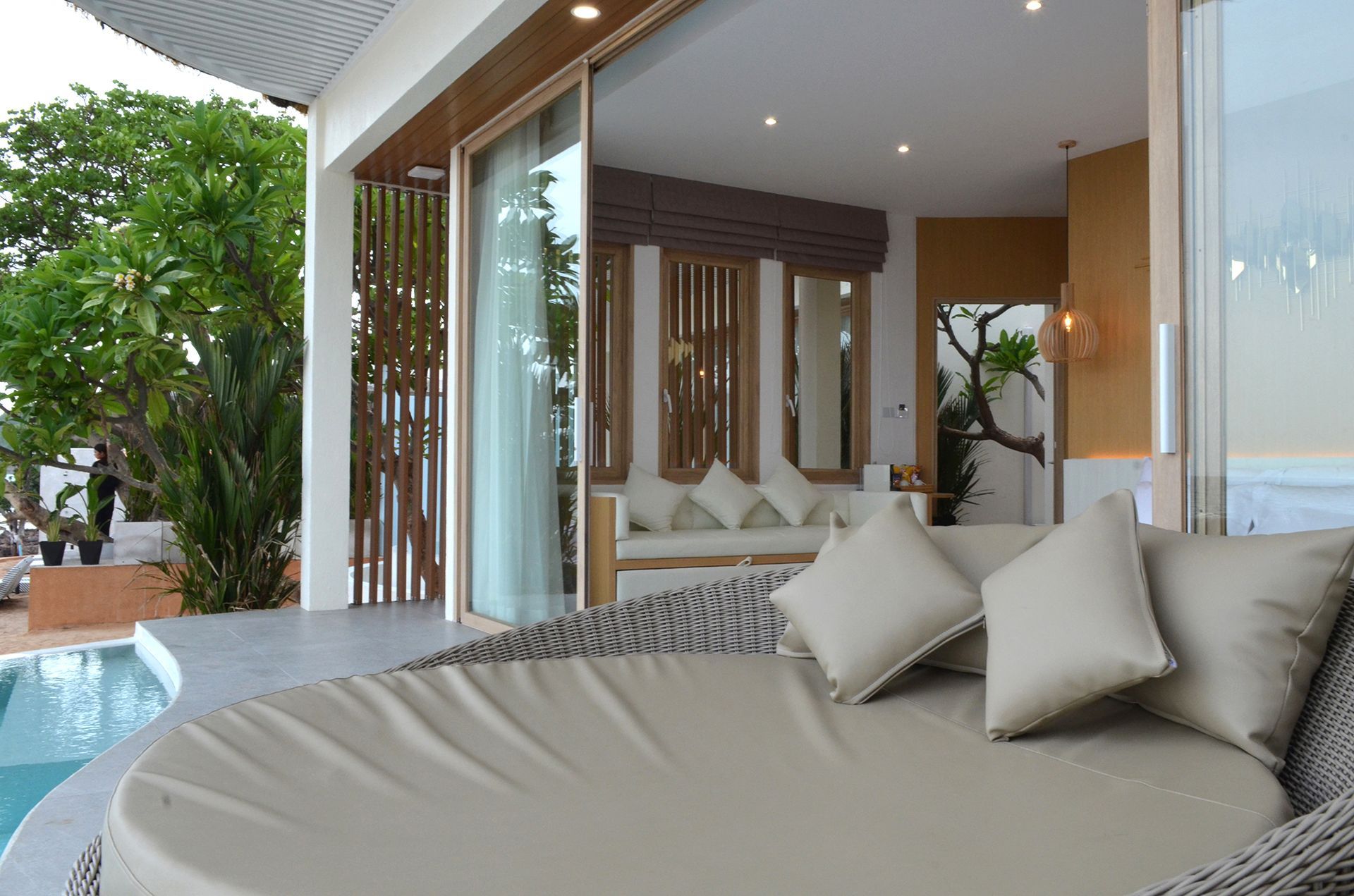 A luxury outdoor patio with a curved daybed, overlooking a pool and interior seating area.
