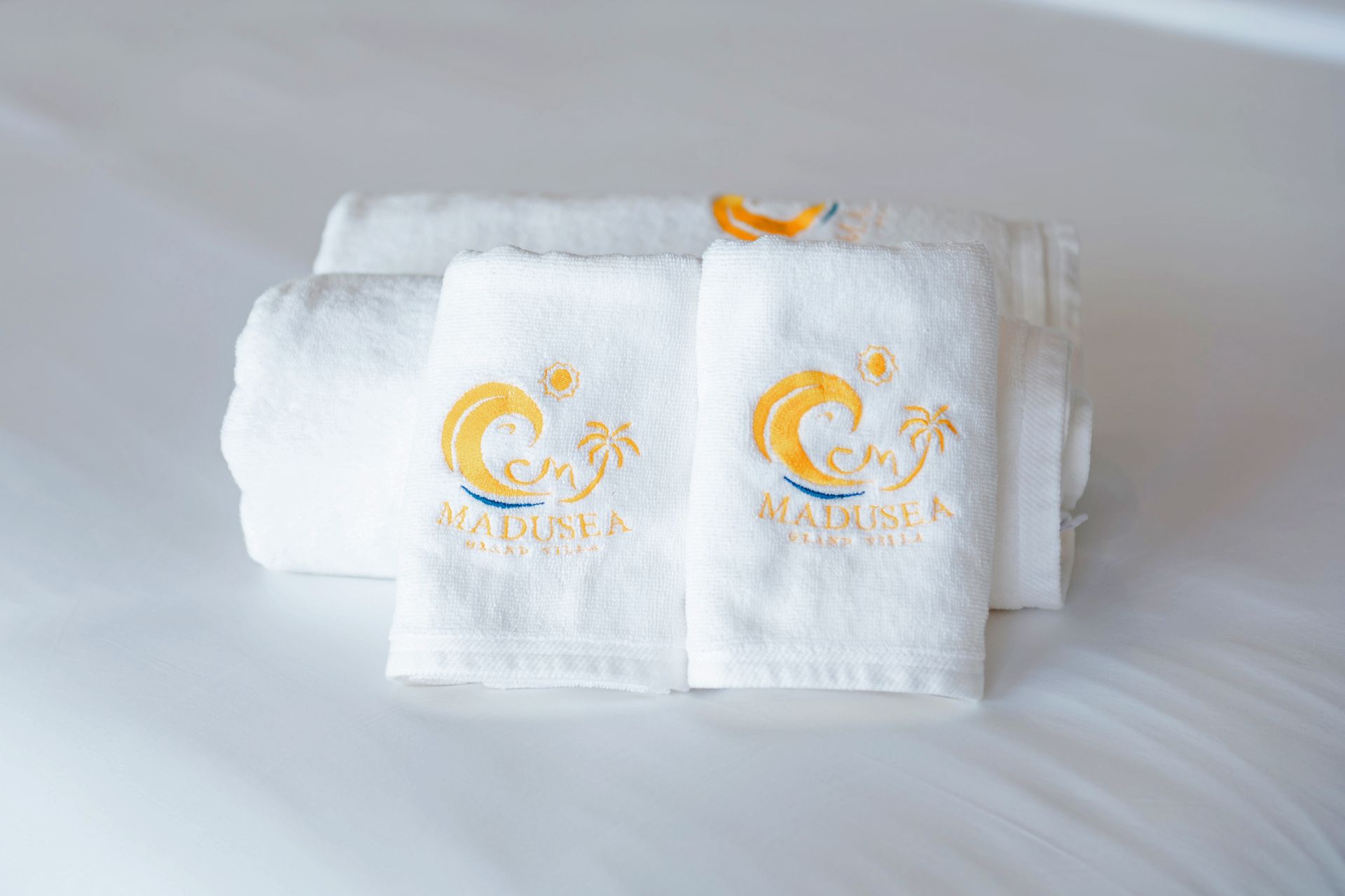 White towels with a yellow and blue logo stacked on a bed.