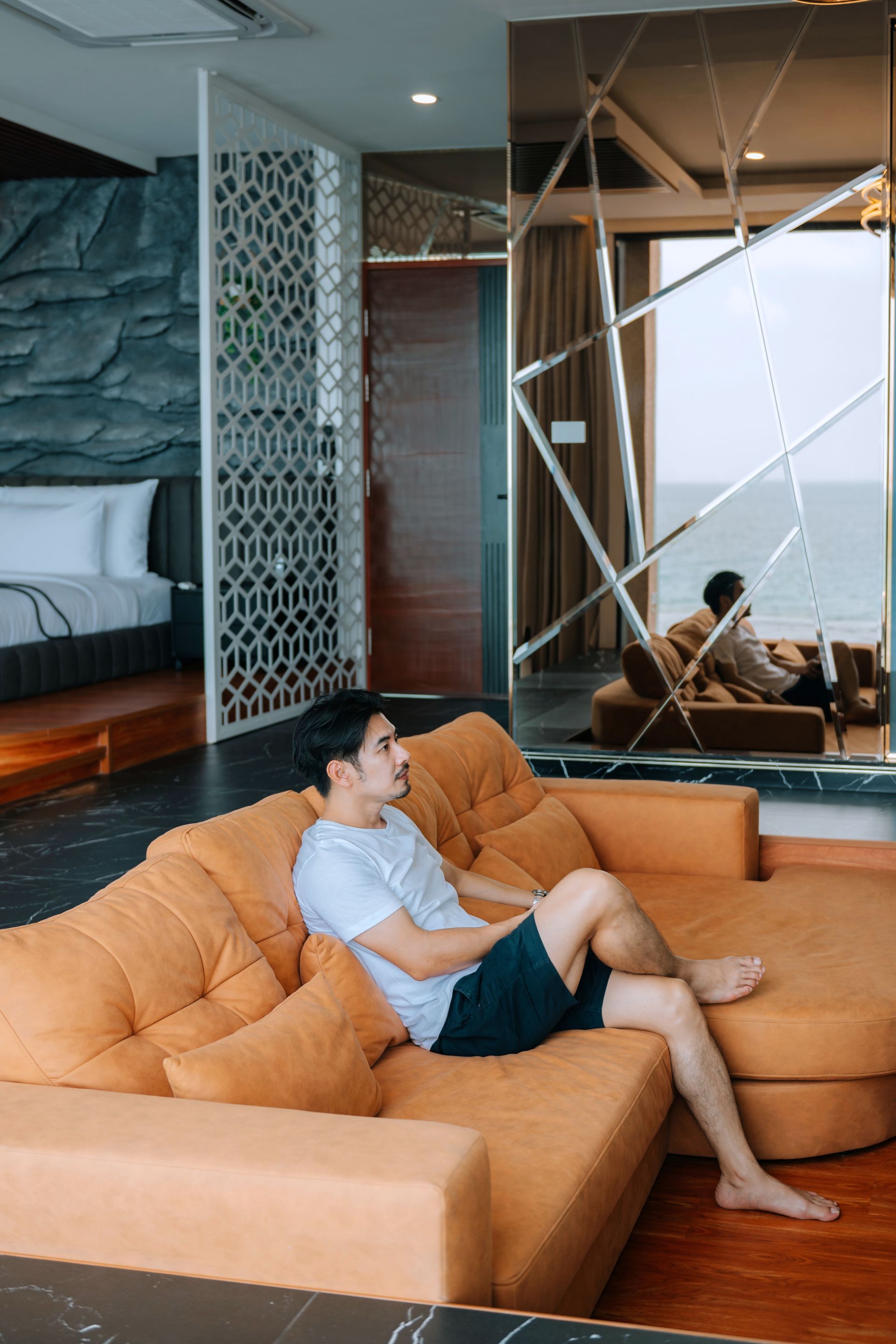 Man relaxes on an orange sectional sofa in a luxury room with a beach view.