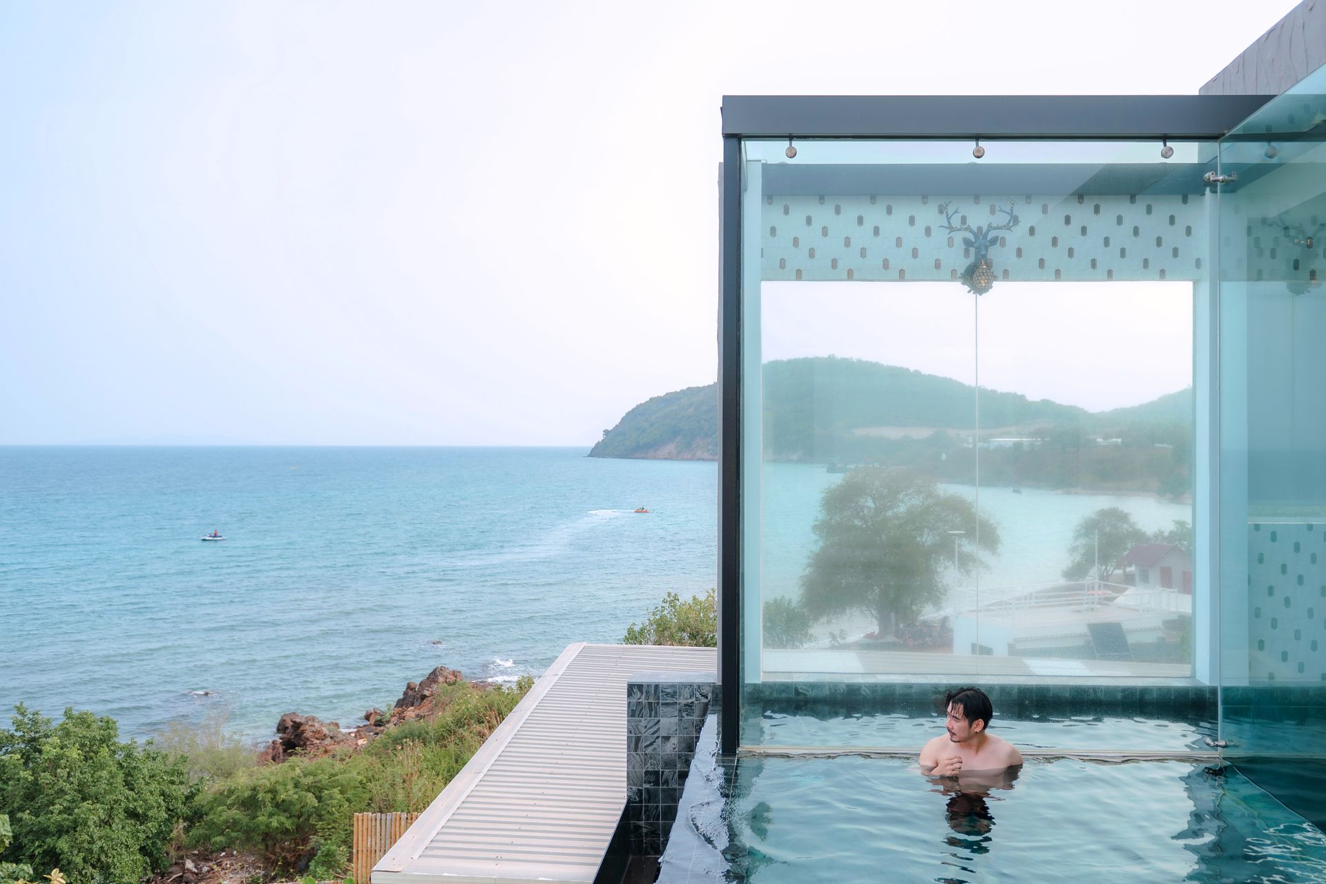 Man in infinity pool looking at the ocean through a glass shower.