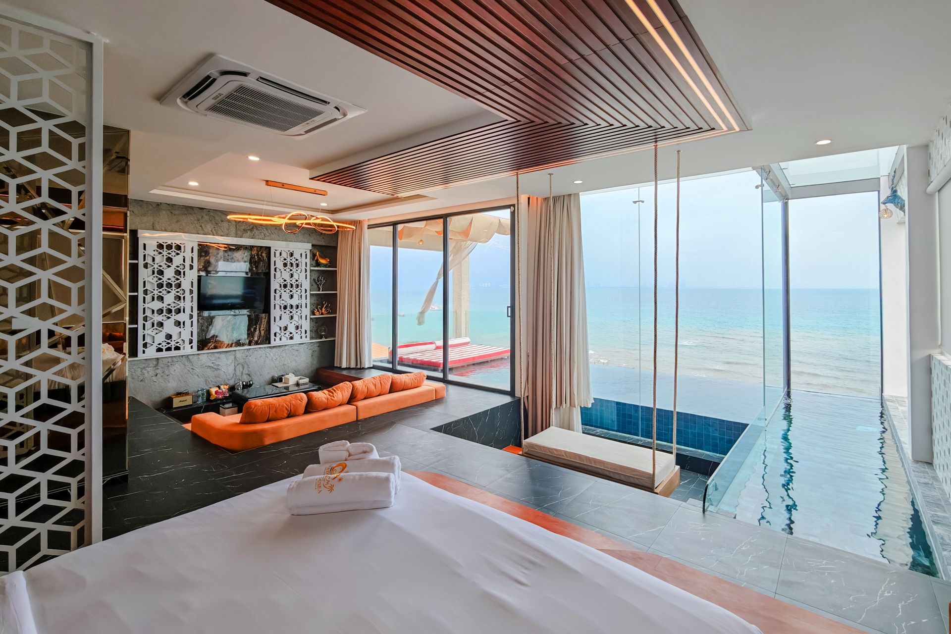 Luxury oceanfront suite with a pool, swing, and an orange sofa.