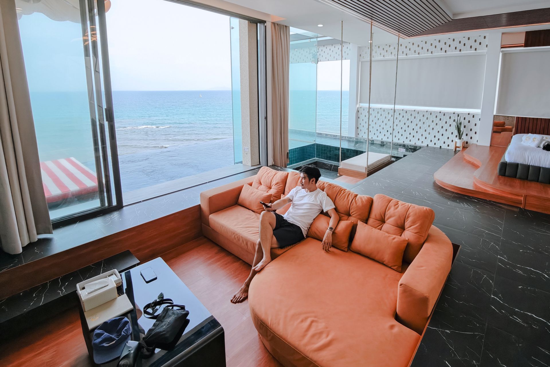 Man relaxing on an orange sofa, ocean view, large window.